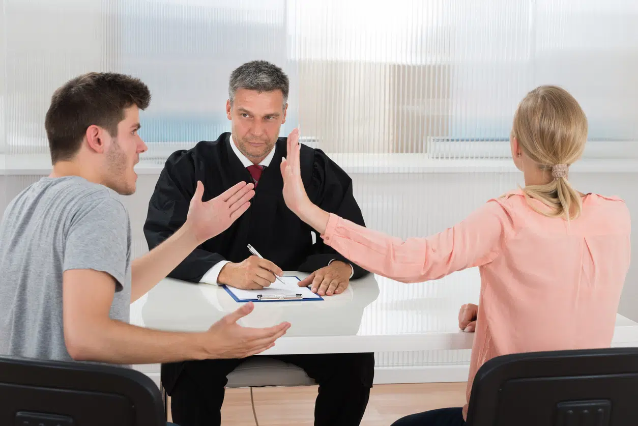 Young Couple Having An Argument In Front Of Male Judge At Desk