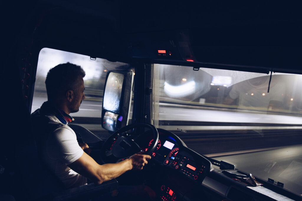 A handsome driver at the wheel of a truck is driving his goods at night. Truck driver job.