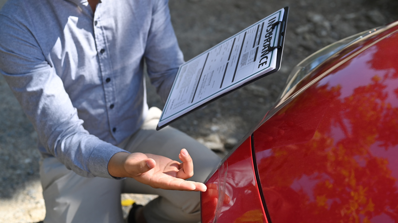 Cropped shot insurance agent holding insurance claim form and inspecting damaged car.