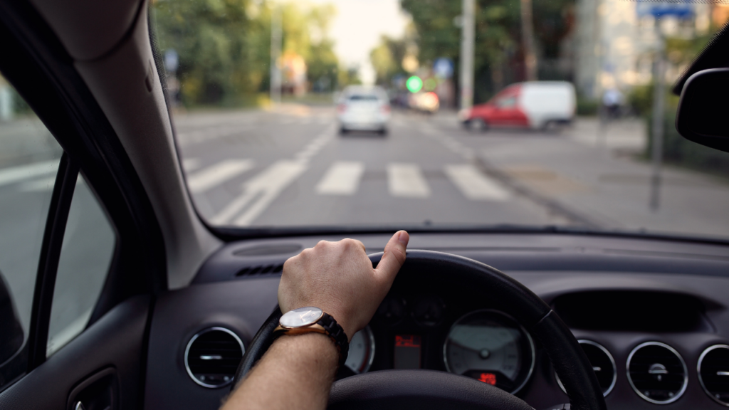 A photo of a person behind the steering wheel near a crosswalk