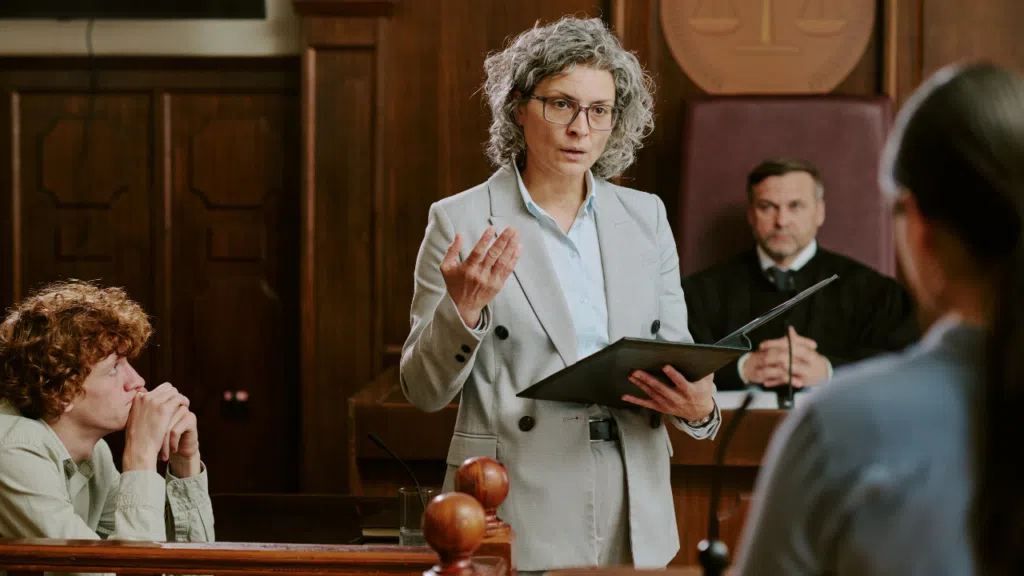 An attorney with the defendant speaking to a judge in a pre-trial conference.